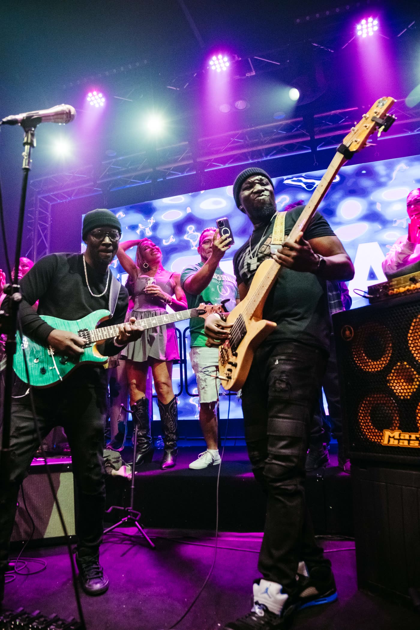 Two guitarists at the front of the Live Room stage against the lit LED wall.
